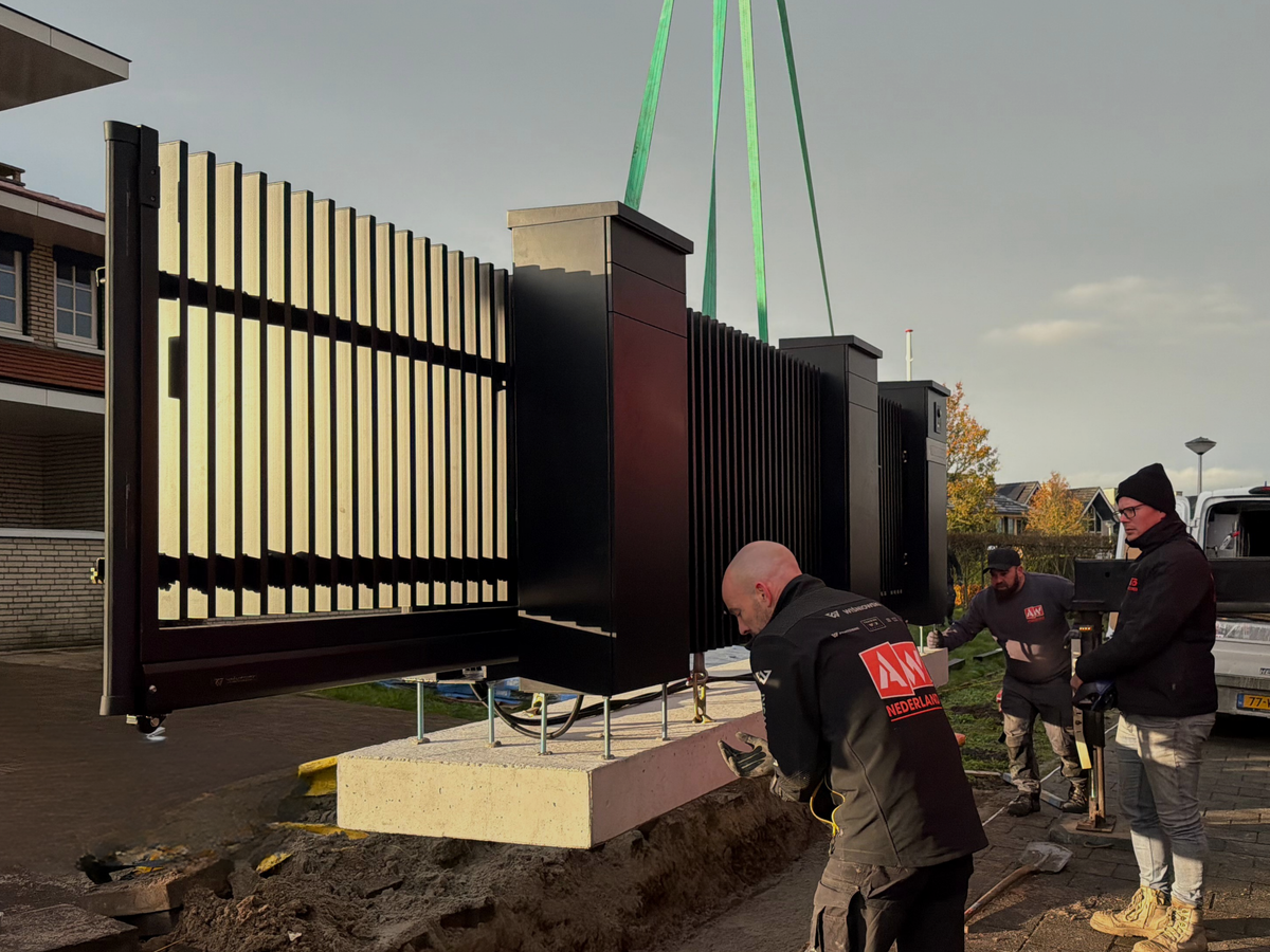 Moderne antraciete schuifpoort met verticale lamellen naast de oprit van een woning